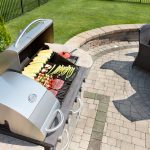 an outdoor grill installed in a grassy backyard with an array of food atop  it
