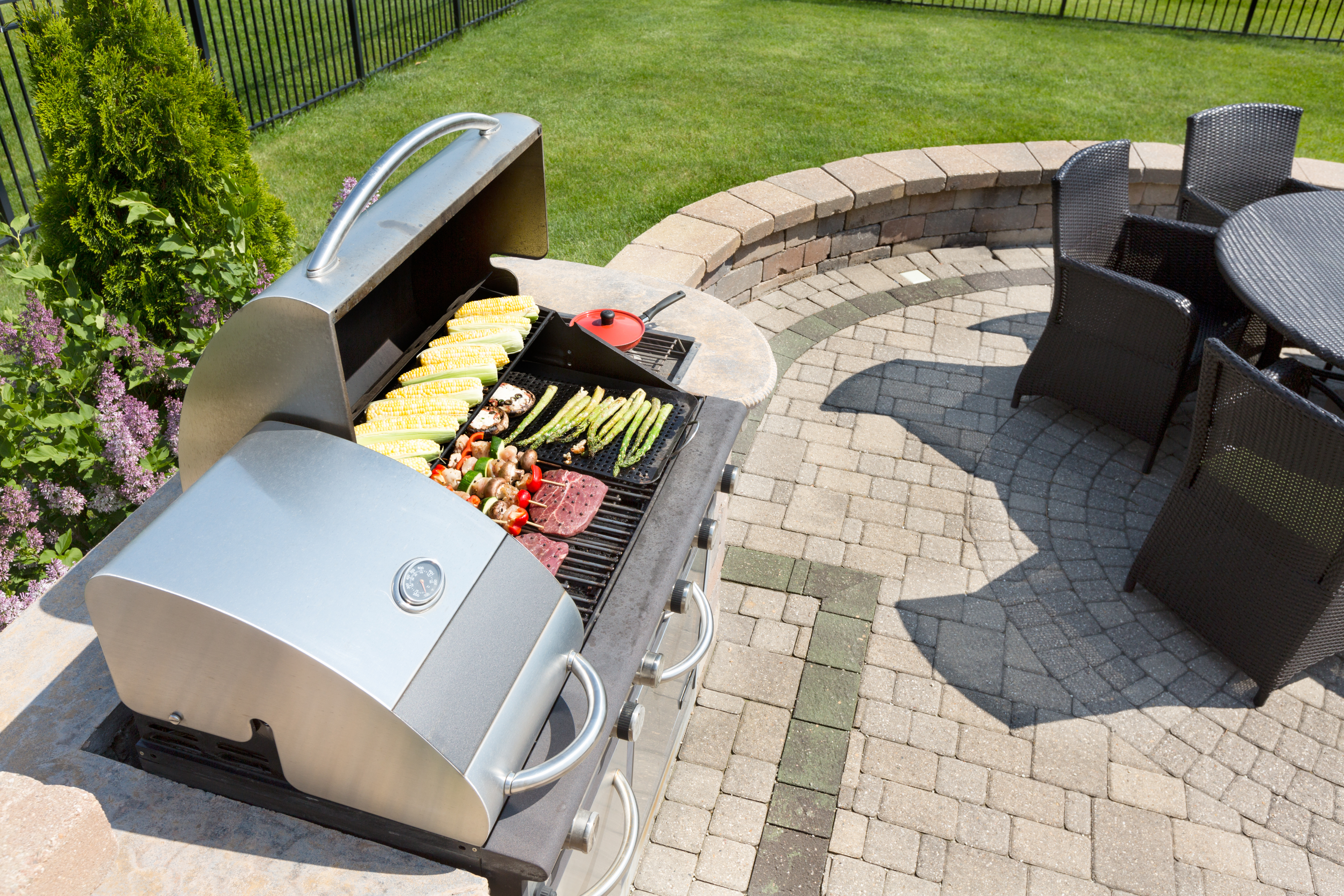 an outdoor grill installed in a grassy backyard with an array of food atop  it