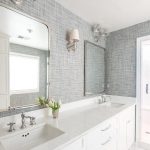 Beautiful white and gray bathroom is clad in gray textured wallpaper  accenting marble herringbone tile floors framing a white dual vanity fitted  with