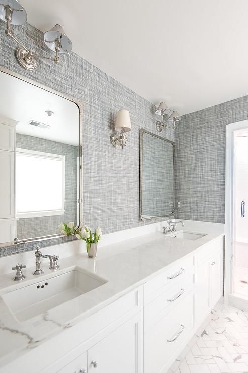 Beautiful white and gray bathroom is clad in gray textured wallpaper  accenting marble herringbone tile floors framing a white dual vanity fitted  with