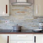 Natural coloured slate wall tiles are used complement this cream modern  kitchen http://