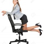 Businesswoman kneeling on office chair, her arms on chair back, looking at  camera cheerfully